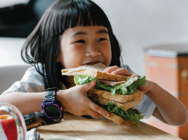  young girl biting into a sandwich